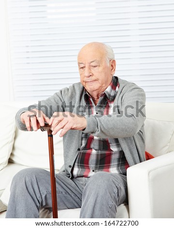 Old man with cane sitting on couch at home