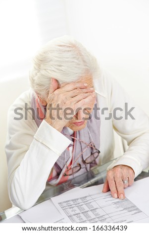 Unhappy senior woman looking at financial bill on the table