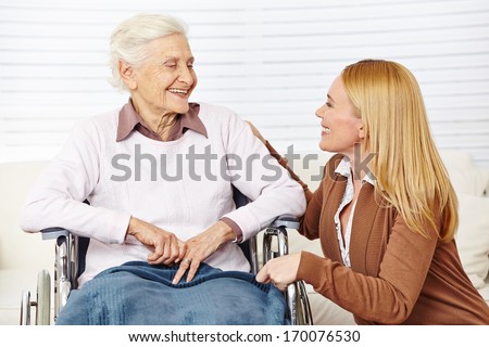 Caregiver Woman Talking To Senior Citizen In Wheelchair At Home