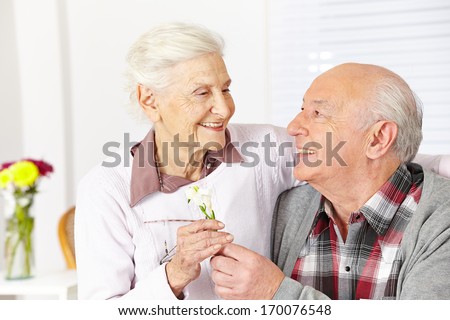 Happy senior citizen giving a freesia flower to smiling woman