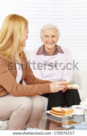Woman and happy senior citizen eating breakfast together in a retirement home