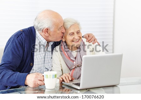 Man kissing happy senior woman at the computer on the cheek