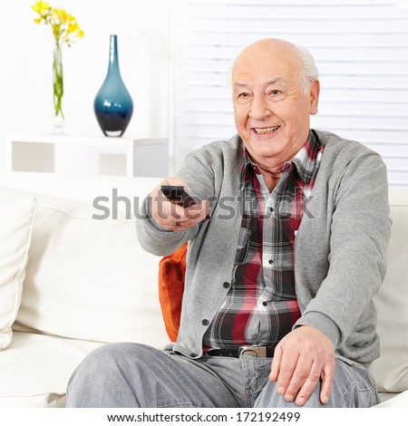 Happy senior citizen man watching TV with remote control