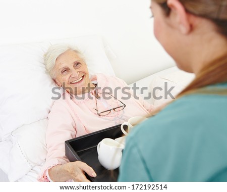 Happy senior woman getting breakfast in bed in a nursing home