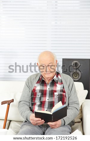 Senior citizen reading a book at home on the sofa