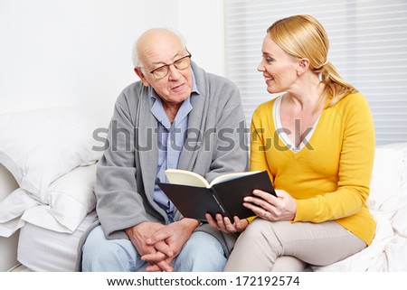 Woman reading a book to a senior citizen man in nursing home