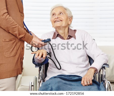 Nurse measuring blood pressure for senior woman in wheelchair in a nursing home