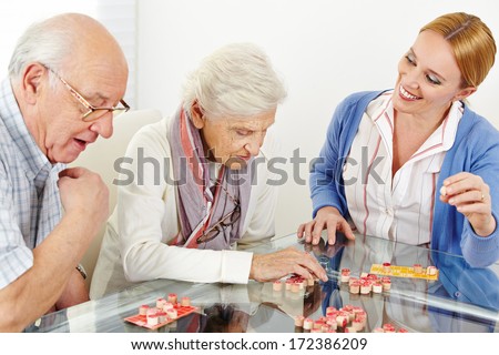 Senior couple playing Bingo with eldercare assistant in nursing home