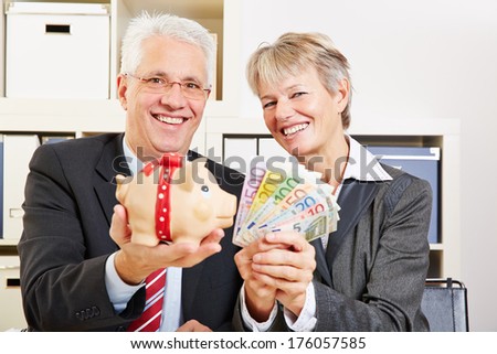 Two senior business people holding Euro money and piggy bank in the office