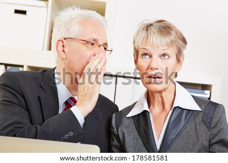 Business man in the office whispering a secret into ear of surprised woman