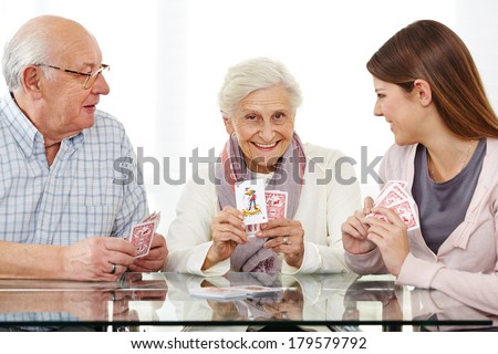 Happy senior couple playing cards with young woman