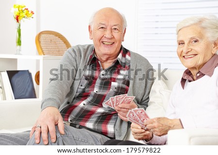 Happy senior citizen couple playing cards at home