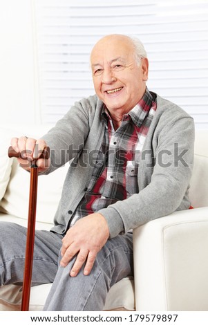 Happy old man with cane sitting at home on a sofa
