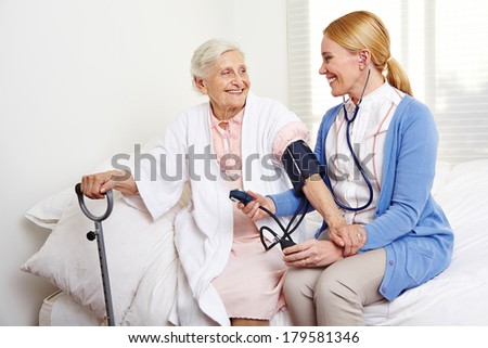 Geriatric nurse measuring blood pressure of senior citizen woman in nursing home