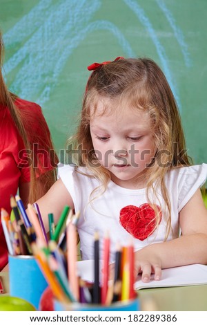 Girl drawing with many colorful crayons in a kindergarten