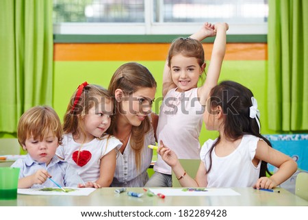 Children talking to nursery teacher in kindergarten while painting pictures