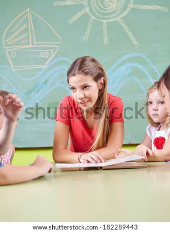 Nursery teacher reading book for children in a kindergarten