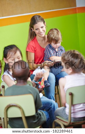 Children in kindergarten sitting in circle and reading book with nursery teacher