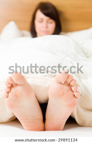 Young woman in her bed with feet outside the blanket