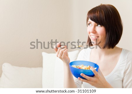 Young woman eating a bowl of muesli in her living room