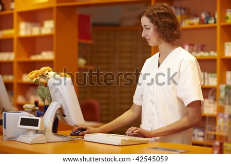 Pharmacist typing on computer behind pharmacy counter
