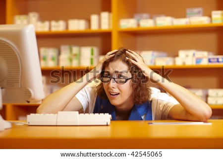Pharmacist looking desperately at computer in pharmacy