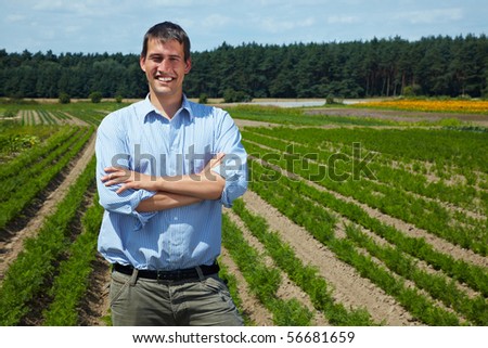 Happy farmer with arms crossed in front of his fields