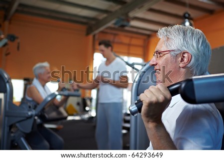 Two senior people working out in a gym with fitness coach