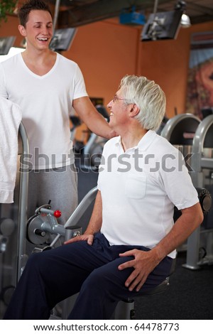 Eldery man doing back exercises in gym with fitness coach