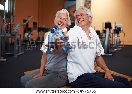 Two happy senior people in a gym drinking water