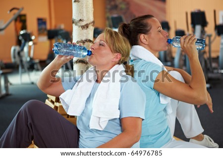 Two happy women in gym taking a break and drinking water
