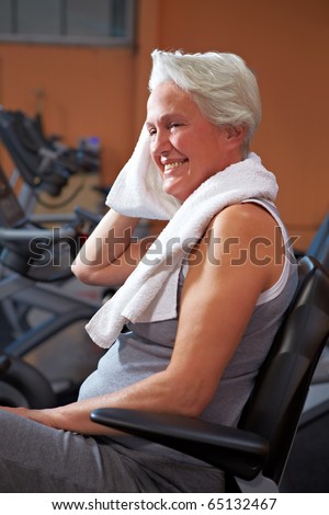 Senior woman sweating in gym and drying herself with towel