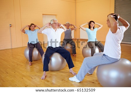 Group doing back exercises with Swiss ball in gym