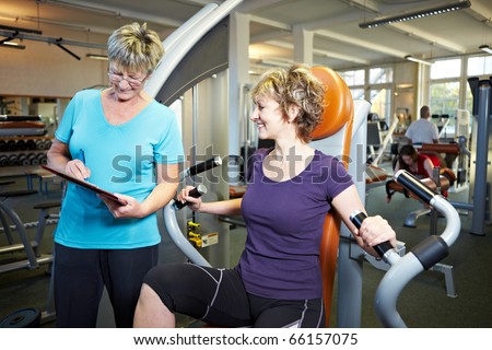 Fitness trainer explaining rowing machine to woman in gym