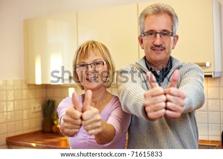 Two happy senior people in kitchen holding thumbs up