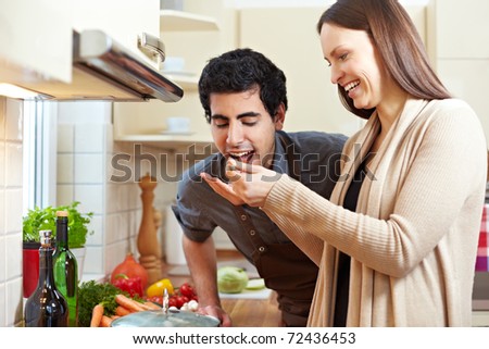 Smiling woman letting man taste a soup with a wooden spoon in the kitchen