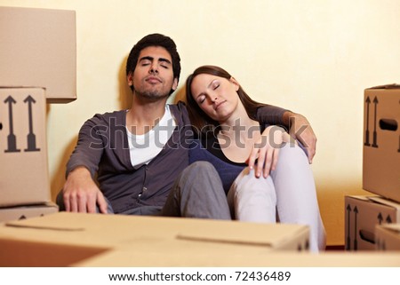 Tired couple sleeping between many boxes in their new home
