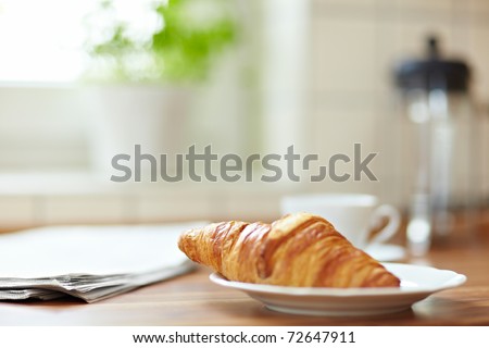 Croissant with newspaper and a cup of coffee on a kitchen counter