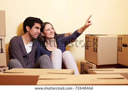 happy couple sitting between many moving boxes and planning their new home