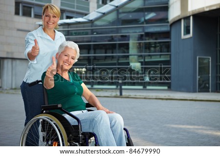 Senior wheelchair driver and nurse holding thumbs up