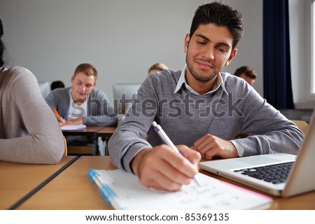 Student with computer taking notes in university class