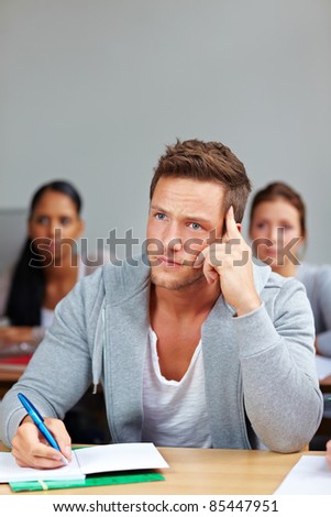 Pensive student thinking and taking notes in university class