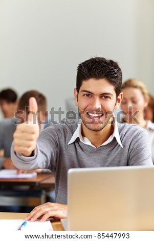 Successful student at laptop holding his thumbs up