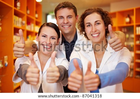 Happy pharmacy team holding their thumbs up in a pharmacy