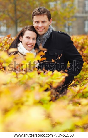 Happy smiling couple behind a hedge in autumn park