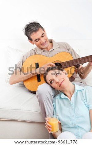 Happy man playing guitar for woman in living room