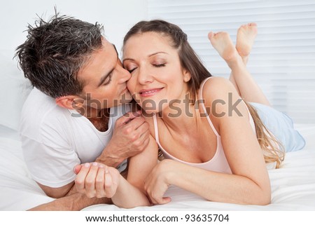 Senior man kissing happy woman in bed