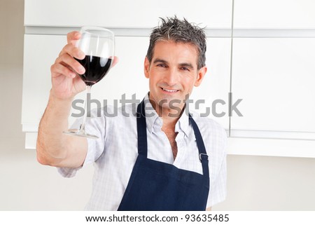 Happy man in kitchen drinking red wine and cheering