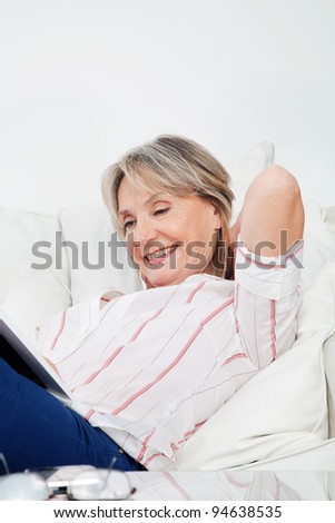 Relaxed senior woman reading a book at home in living room