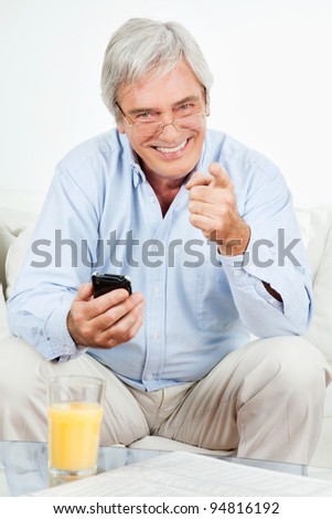 Smiling senior man with smartphone at home on couch